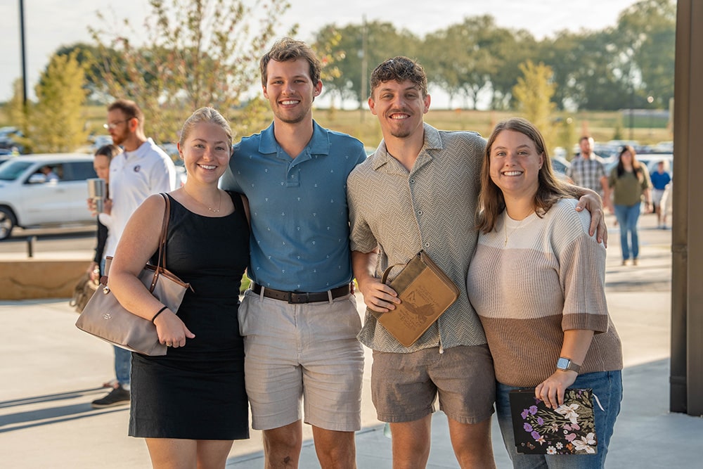 A group of young people smile together while holding their Bibles outside the church