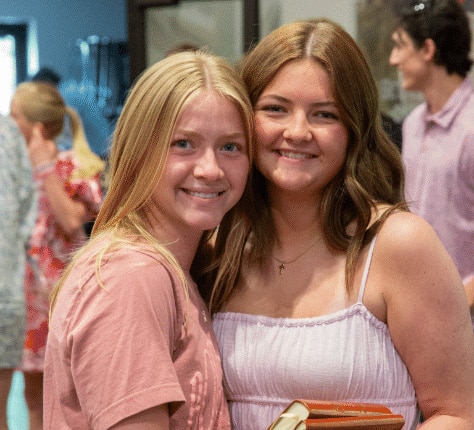 Two teenage girls hug while smiling for a photo